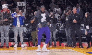 a man is dancing on a basketball court in front of a crowd while holding a sign that says lakers