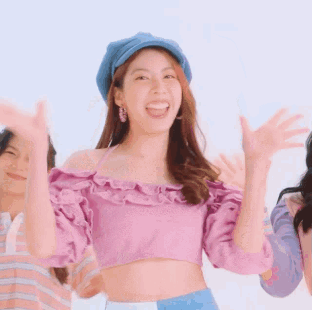 a woman in a purple crop top and a blue hat is smiling