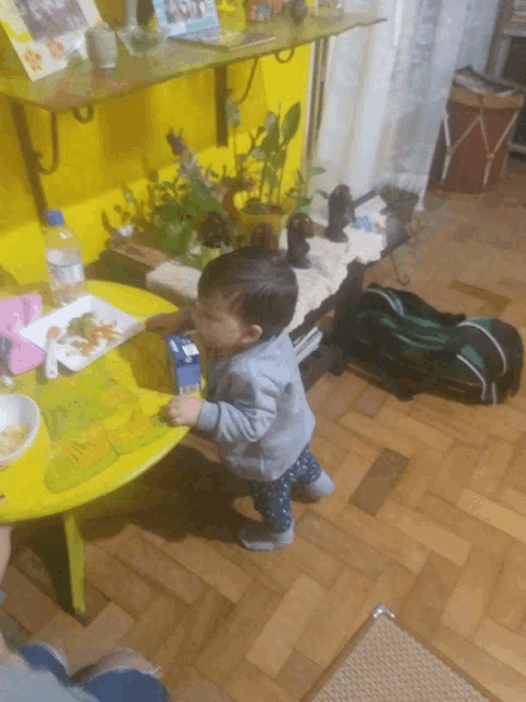 a little boy standing in front of a yellow table with a box of milk