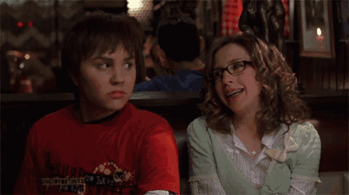 a boy wearing a red shirt that says ' the city of angels ' on it sits next to a woman wearing glasses