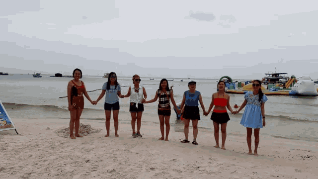 a group of women standing on a beach holding hands with one wearing a shirt that says ' i love you ' on it