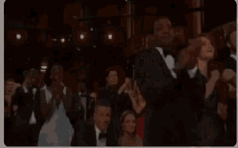 a group of people are sitting in a theatre clapping their hands .