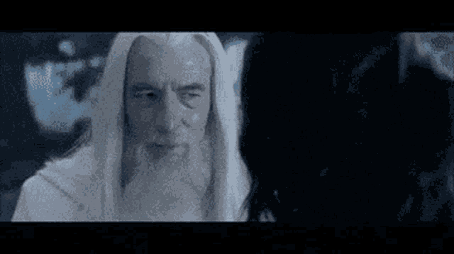 a man with a white beard is talking to a woman in a dark room