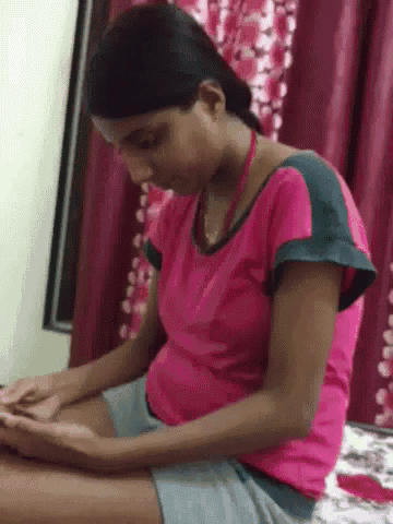 a woman in a pink shirt and shorts is sitting on a bed and looking at her phone .