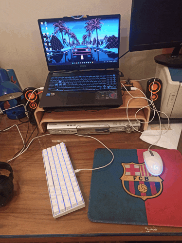 a laptop sits on top of a wooden desk next to a mouse pad that says fcb