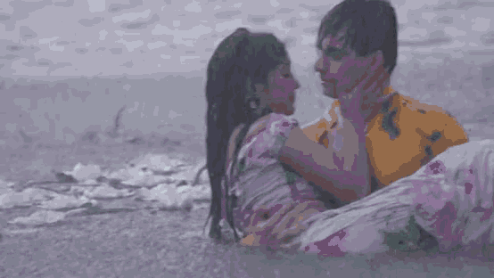 a man is holding a woman in his arms while they are kissing in the water .