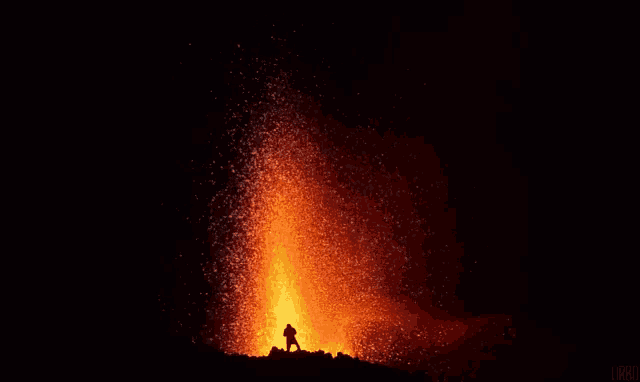 a man is standing in front of a large volcano at night