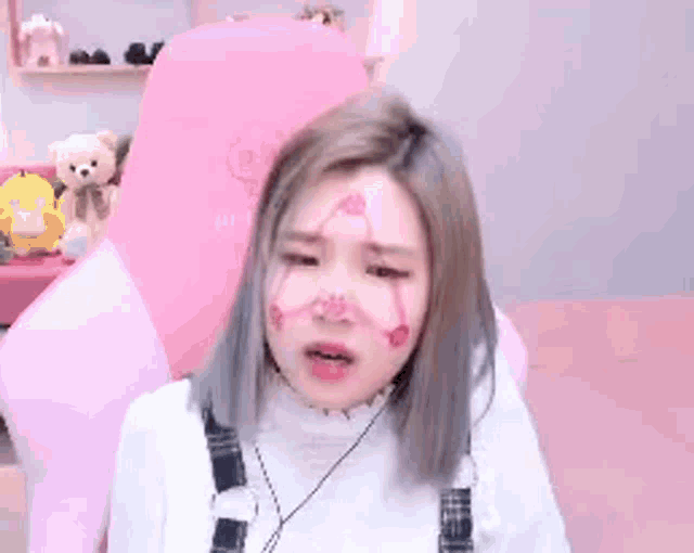 a woman with pink paint on her face is sitting in front of a pink chair .