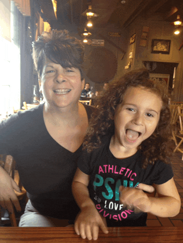 a woman and a little girl are posing for a picture and the little girl is wearing an athletic psw shirt