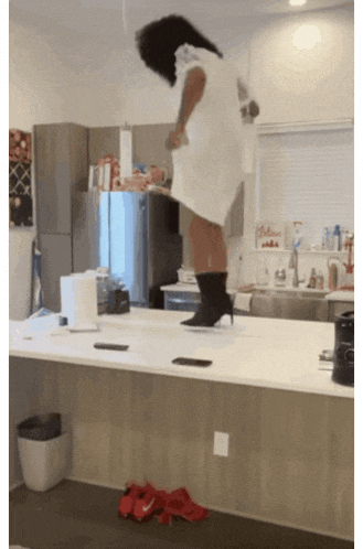 a woman in a white dress and black boots is standing on a kitchen counter