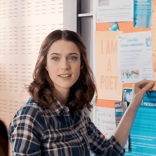 a woman in a plaid shirt points to a poster that says i am a poet on it