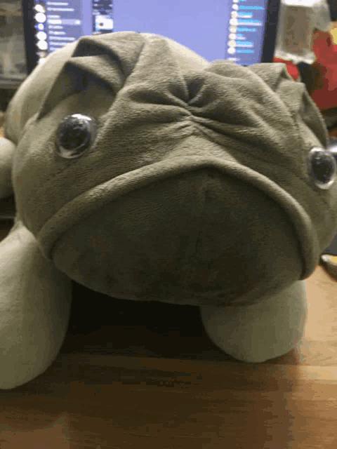 a stuffed pug is laying on a desk in front of a computer monitor