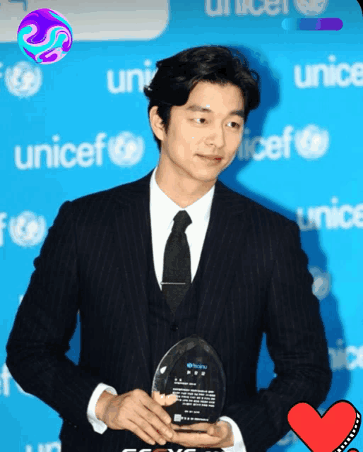 a man in a suit and tie holding a plaque in front of a unicef sign