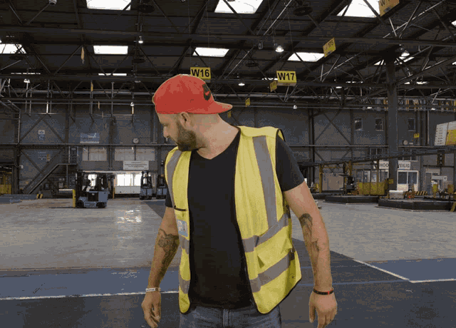 a man wearing a red hat and a yellow vest is standing in a warehouse with a sign that says w16