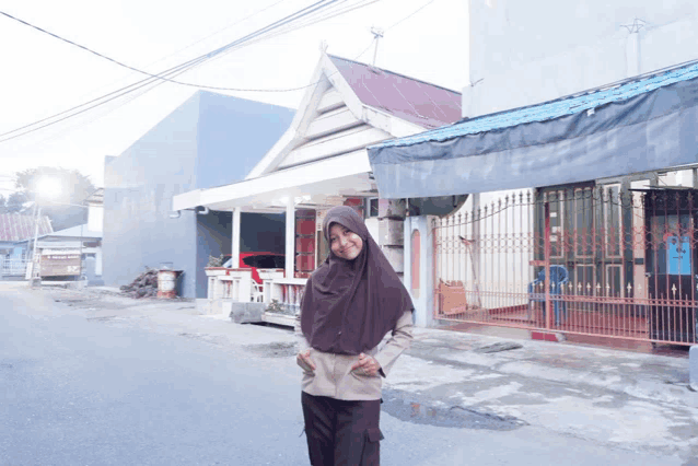 a girl in a hijab stands in front of a house