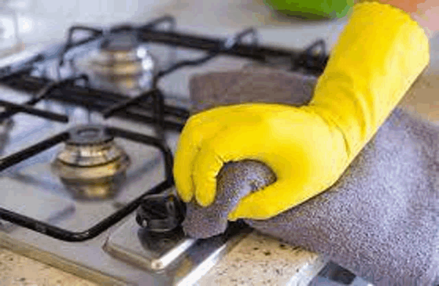 a person wearing yellow rubber gloves is cleaning a stove top with a towel and sponge .