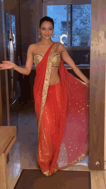 a woman in a red and gold sari is standing in a doorway