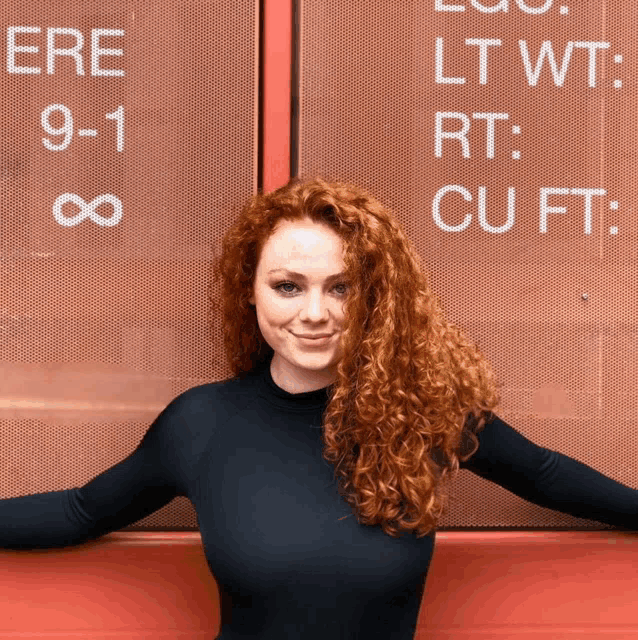 a woman with red hair is standing in front of a sign that says ere 9-1 lt wt rt cu ft