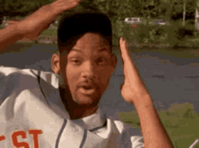 a man in a baseball uniform is standing in front of a river with his hands in the air .