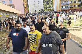 a group of men are walking down a sidewalk in front of a large crowd of people .