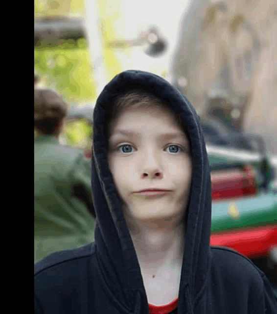 a young boy wearing a black hoodie looks at the camera with a blurry background