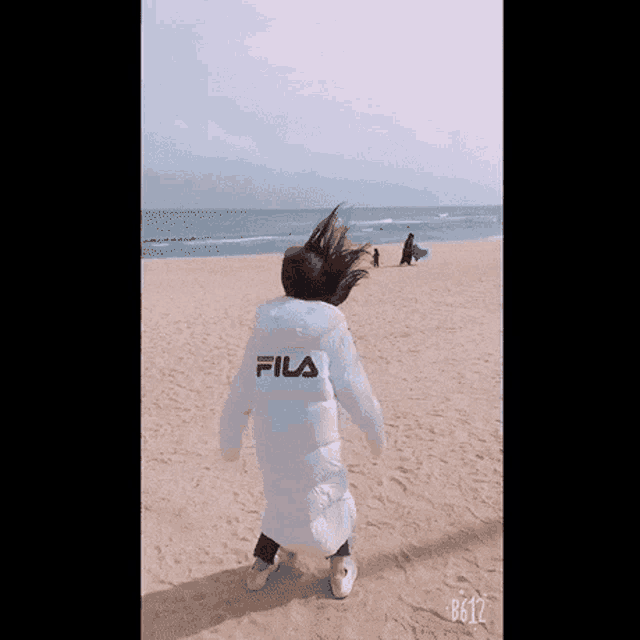 a person wearing a fila jacket is standing on a beach