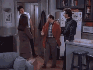 a group of people are standing in a living room talking to each other
