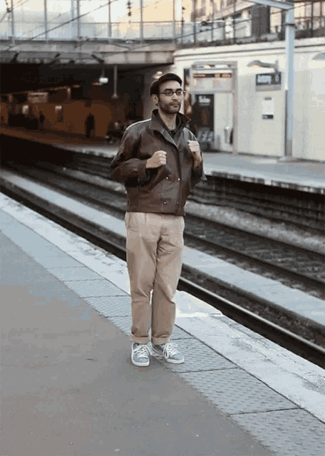 a man in a brown jacket stands on a train platform with a sign that says ' a ' on it