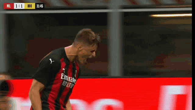 a man in a black and red jersey is standing in front of a red sign that says mil on it