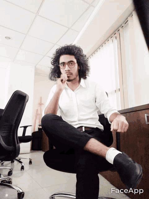 a man in a white shirt and black pants is sitting in an office chair with his leg up and the word face app visible