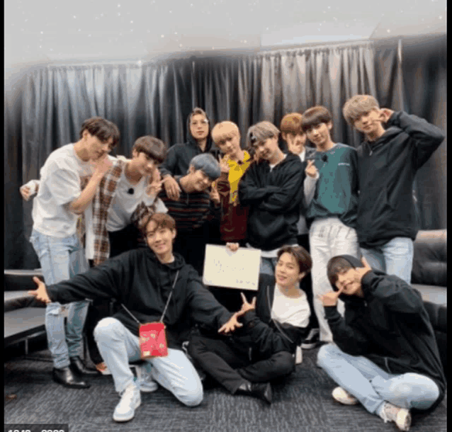 a group of young men are posing for a picture and one of them is holding a sign that says ' bts '