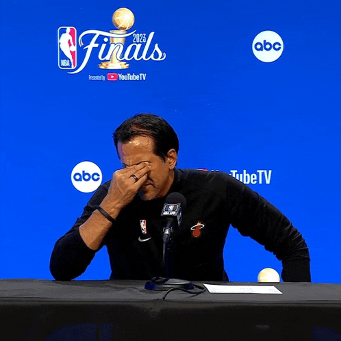 a man covering his eyes while sitting at a table in front of a sign that says finals