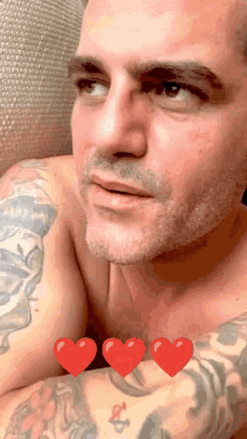 a shirtless man with a tattoo on his arm has three red hearts on his chest