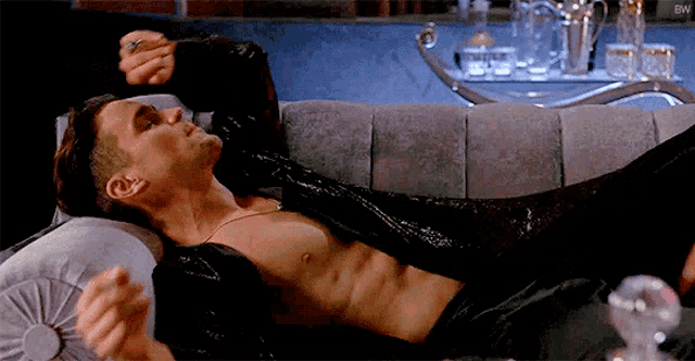 a shirtless man is laying on a couch with his arms outstretched .