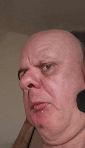 a close up of a bald man 's face with a piercing on his lip