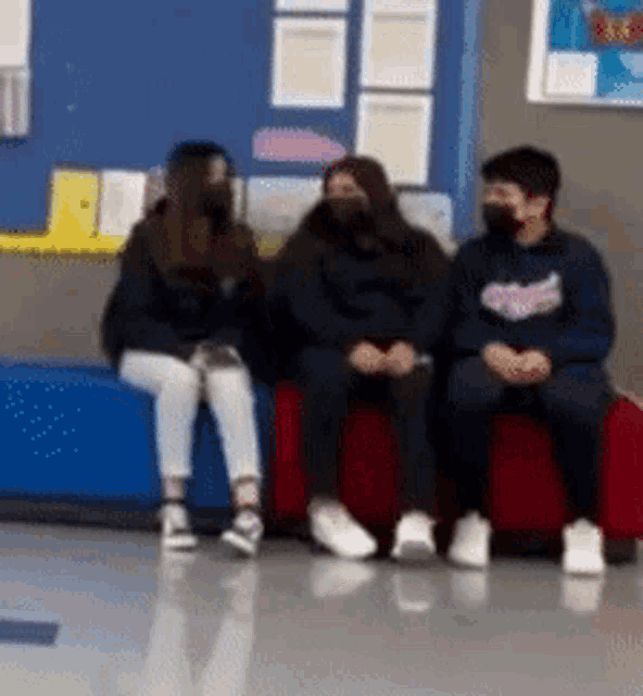 three people wearing masks are sitting on a couch