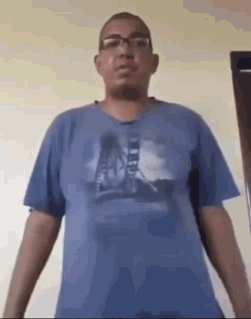 a man wearing glasses and a blue t-shirt is standing in front of a door .