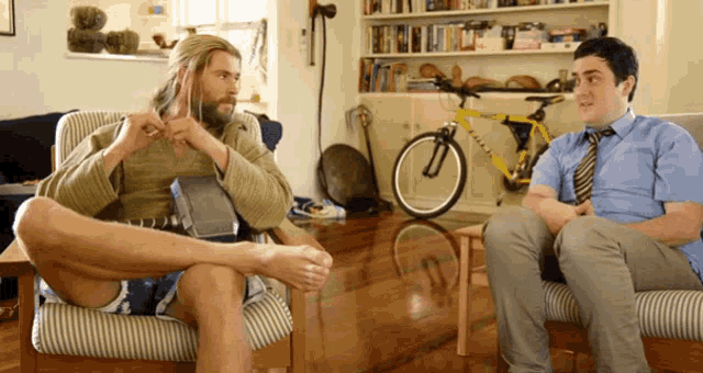 two men are sitting in chairs in front of a bicycle