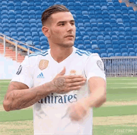 a soccer player in a white emirates jersey is standing on a field with his hands on his chest .