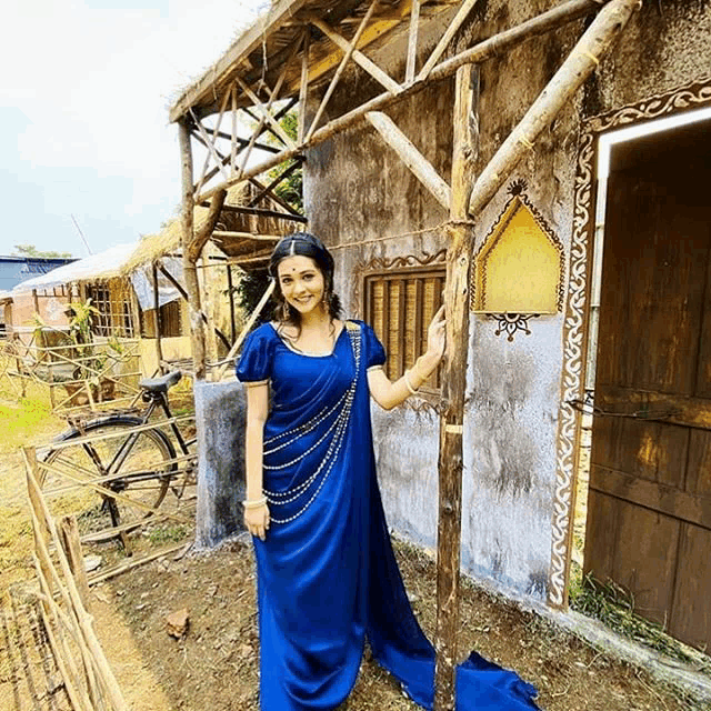 a woman in a blue dress stands in front of a wooden building