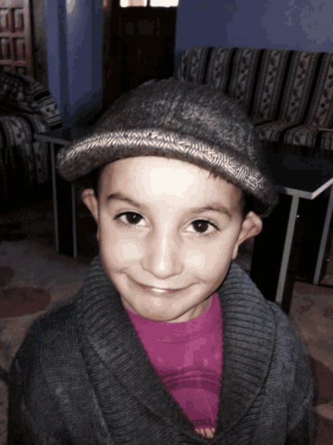 a young boy wearing a hat and a sweater smiles