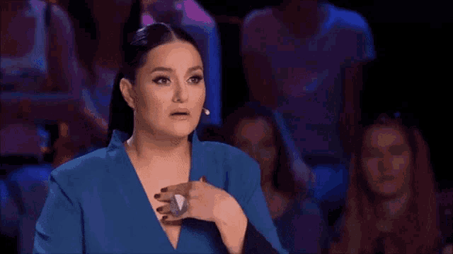 a woman in a blue dress is making a funny face in front of a crowd of people .