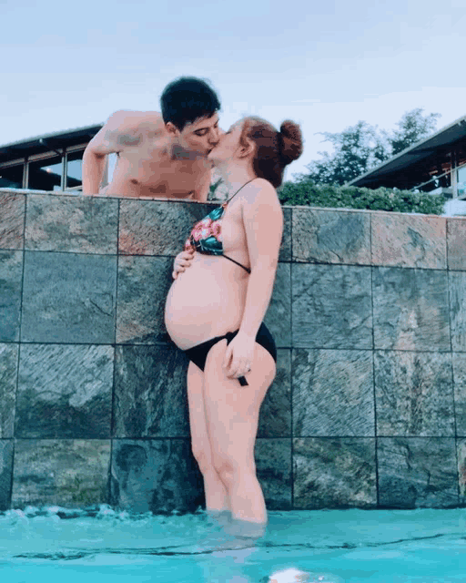 a man kissing a pregnant woman in a bikini in a pool