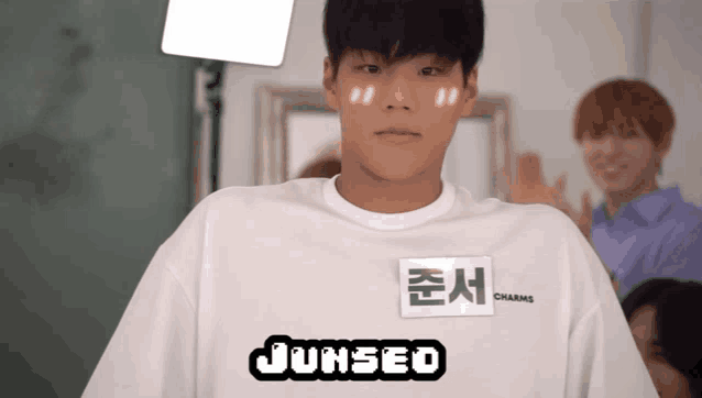 a young man wearing a white shirt that says junseo charms