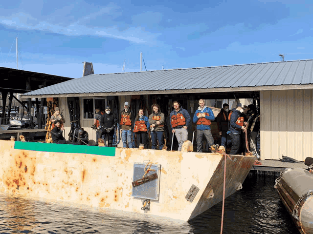 a group of people standing on a boat in front of a building with a sign that says ' a ' on it