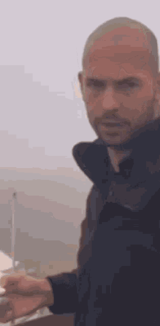 a man with a beard and a bald head is standing in front of a boat .