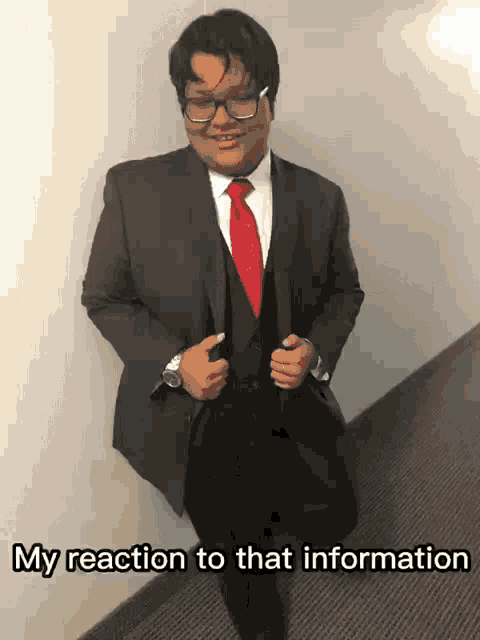a man in a suit and red tie is standing in a hallway with the caption my reaction to that information