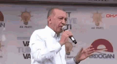 a man in a white shirt is singing into a microphone in front of a sign that says ak parti .