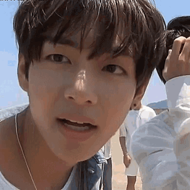 a close up of a young man 's face while standing on a beach with a group of people .