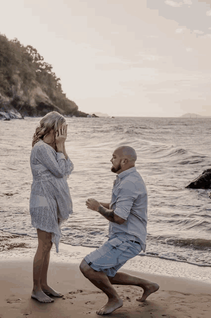 a man kneeling down to propose to a woman on a beach